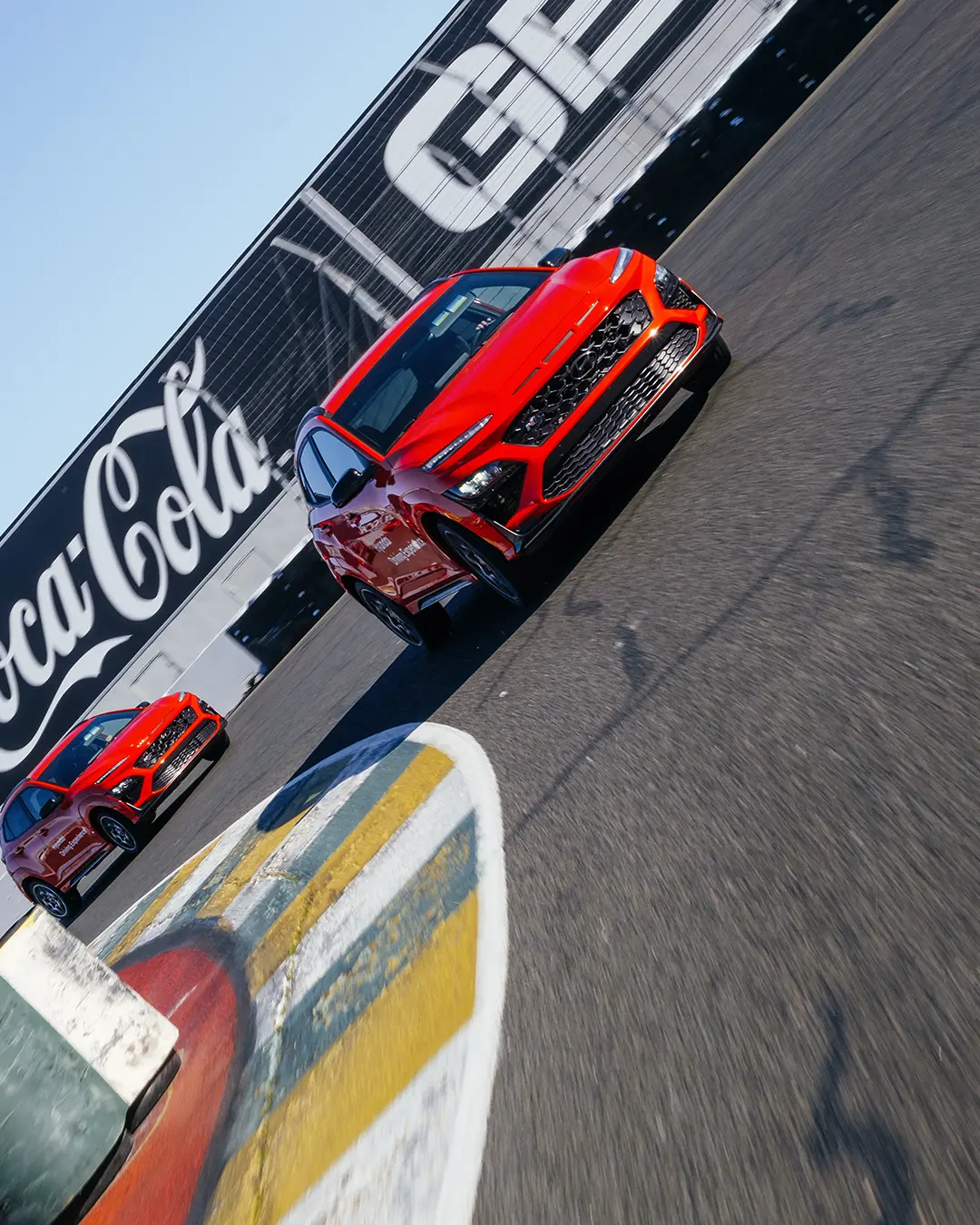 Zwei rote Hyundai Kona, die auf der Rennstrecke schnell um eine Kurve fahren.